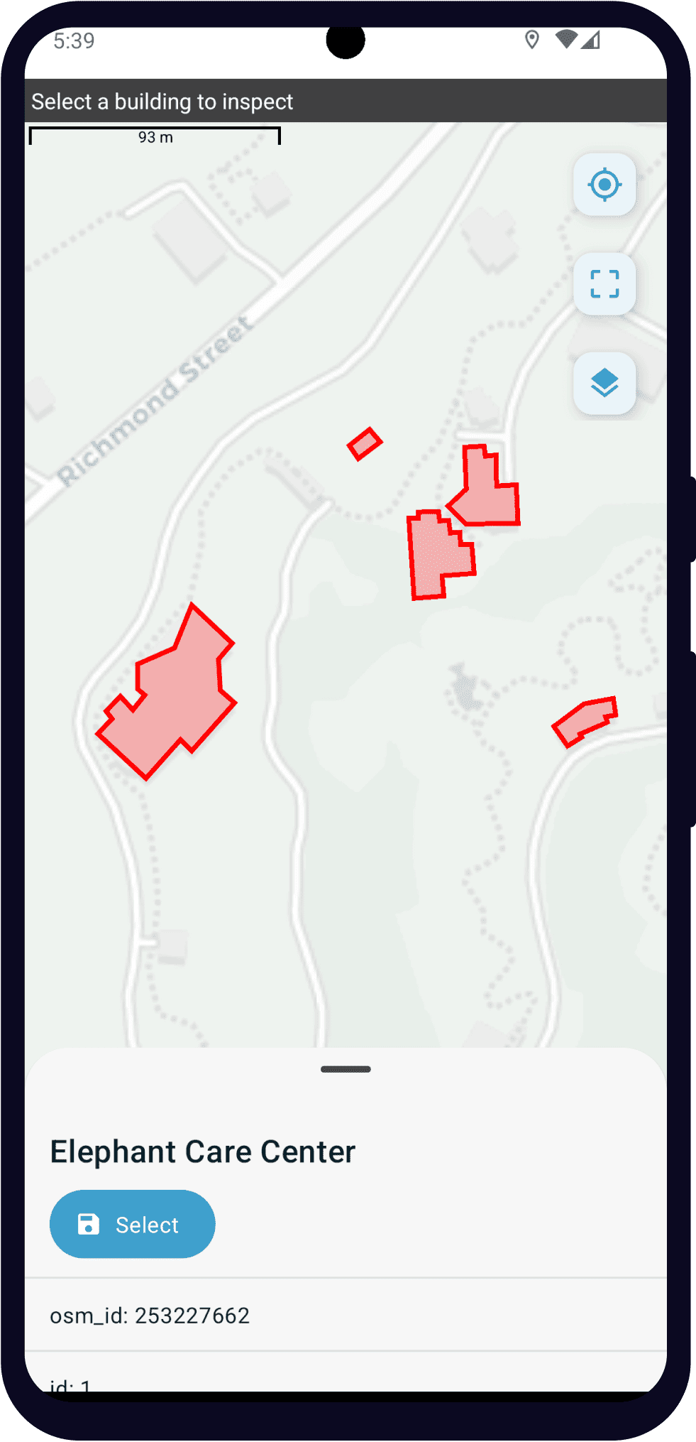 Single select from map as displayed in the ODK Collect app on an Android phone. The question text is "Select a building to inspect" and it is displayed in a small top bar. Below that is a map with several buildings outlined in red with red shading. At the bottom of the screen, there is information about the selected building. Its label is "Elephant Care Center". Below the properties, there is a rounded button with a save icon and the text "Select."